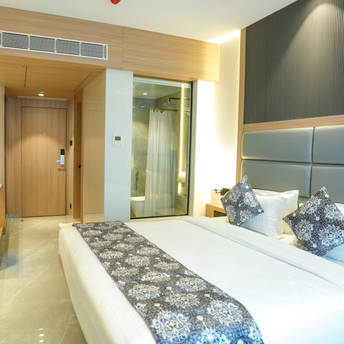 Modern hotel bedroom with neutral tones and glass-walled bathroom