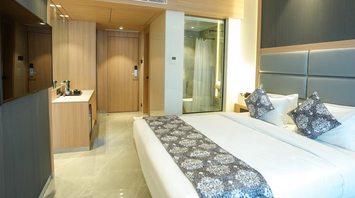 Modern hotel bedroom with neutral tones and glass-walled bathroom