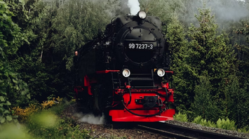 Black and red steam locomotive traveling through a forested railway curve on a misty day