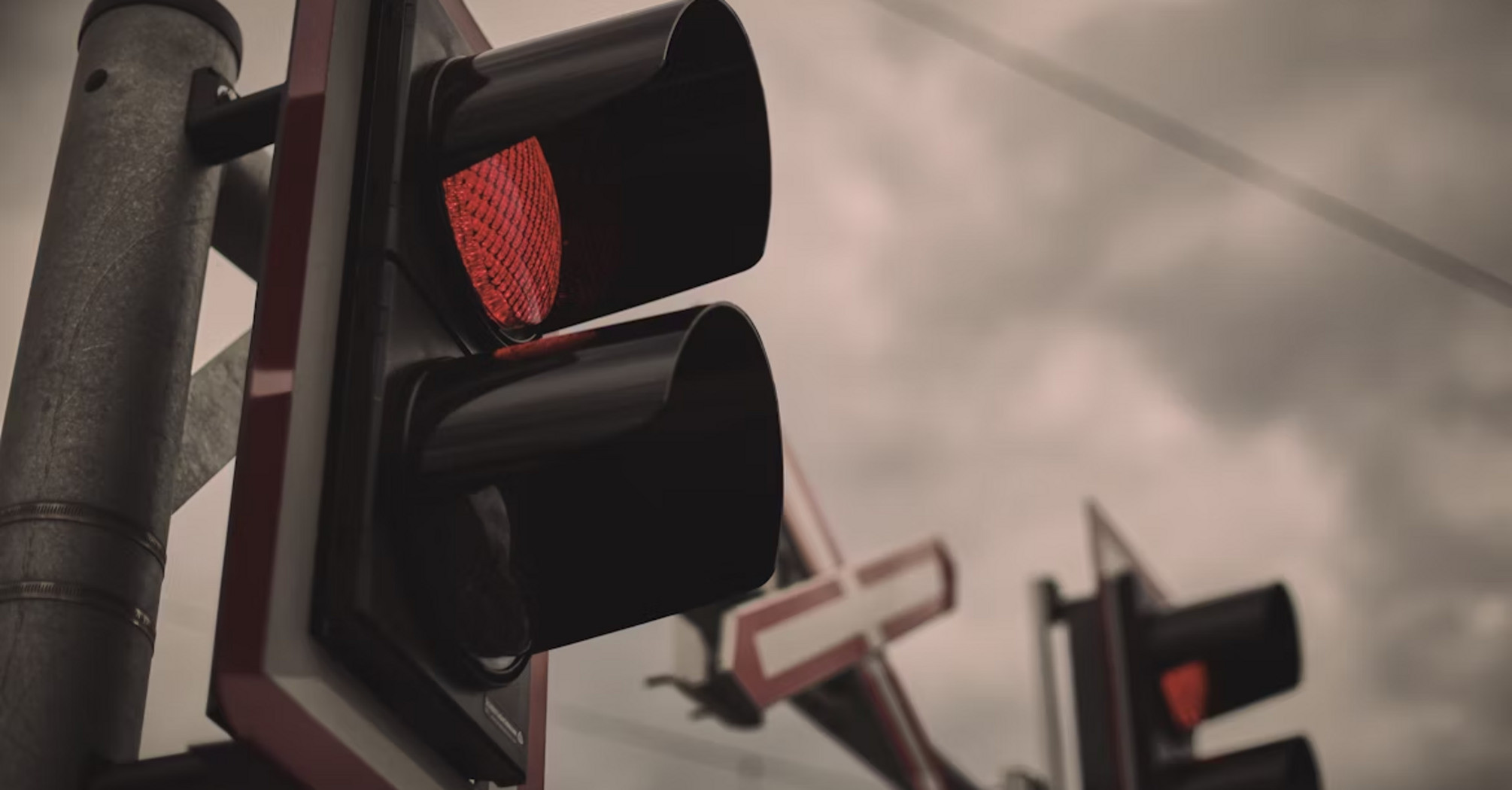 Red railway crossing signal with barriers lowered under cloudy sky