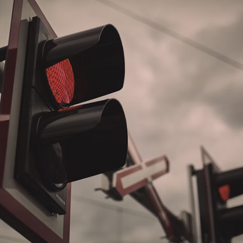 Red railway crossing signal with barriers lowered under cloudy sky
