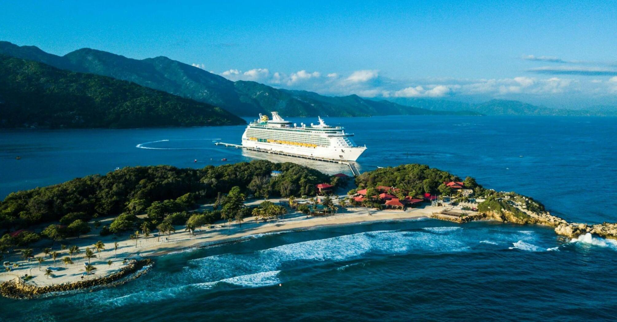 Cruise ship docked at a Caribbean island with lush hills and turquoise waters