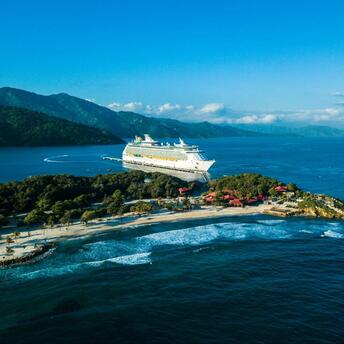 Cruise ship docked at a Caribbean island with lush hills and turquoise waters