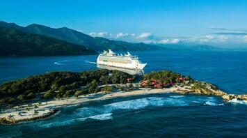 Cruise ship docked at a Caribbean island with lush hills and turquoise waters