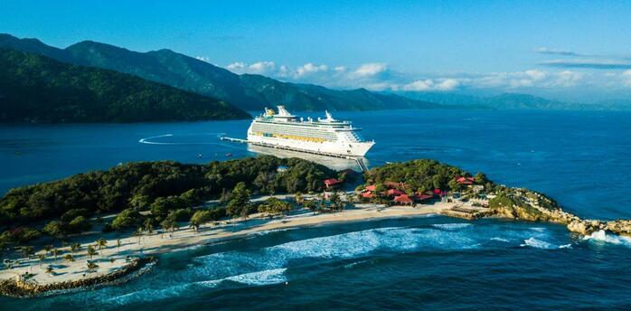Cruise ship docked at a Caribbean island with lush hills and turquoise waters