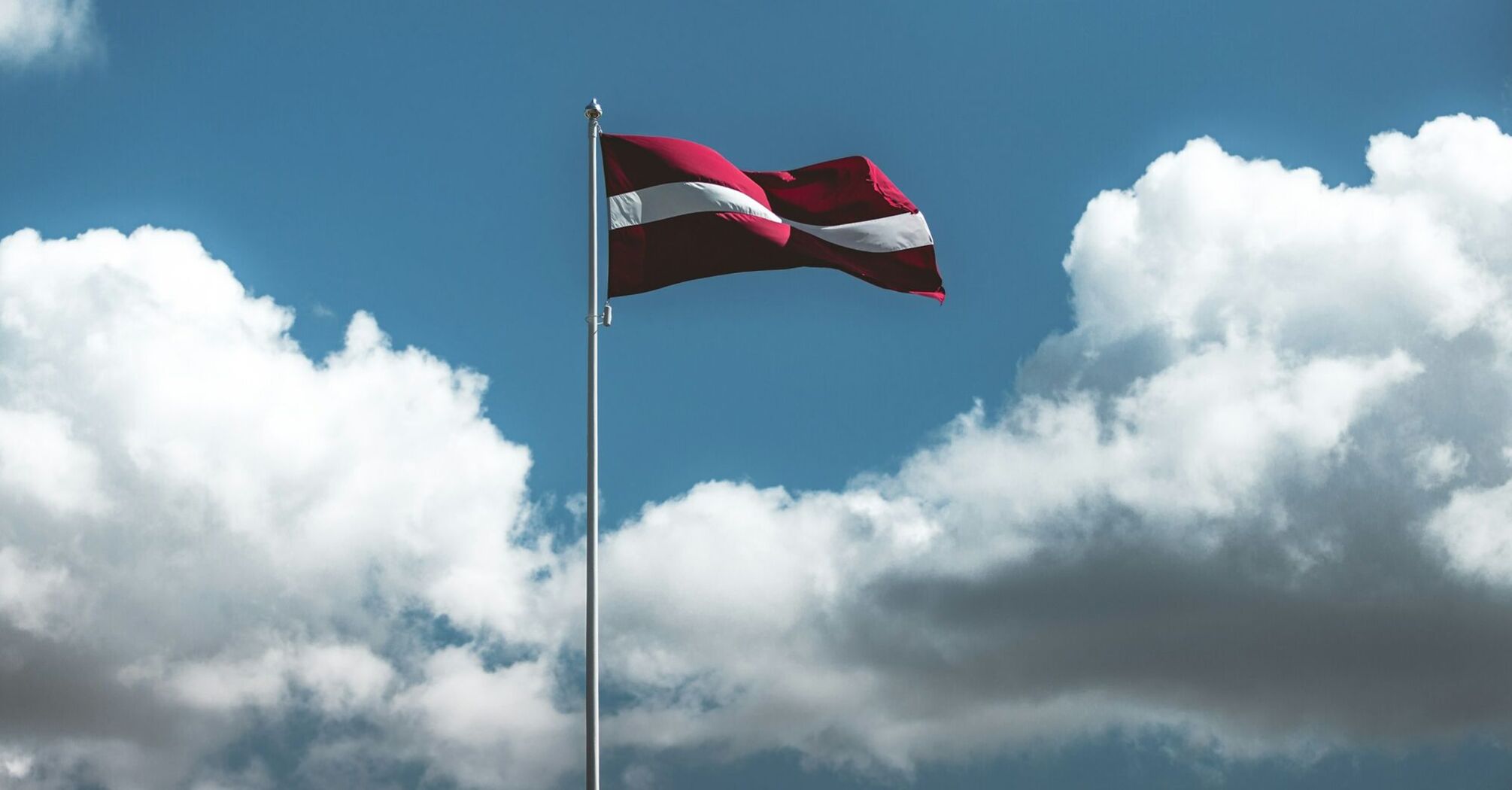 Latvian national flag flying high against clouds