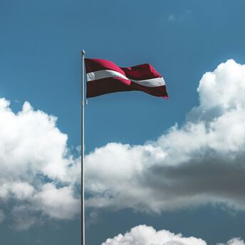 Latvian national flag flying high against clouds