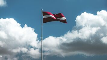Latvian national flag flying high against clouds