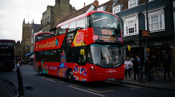 Red double-decker sightseeing bus on a Cambridge street with people nearby