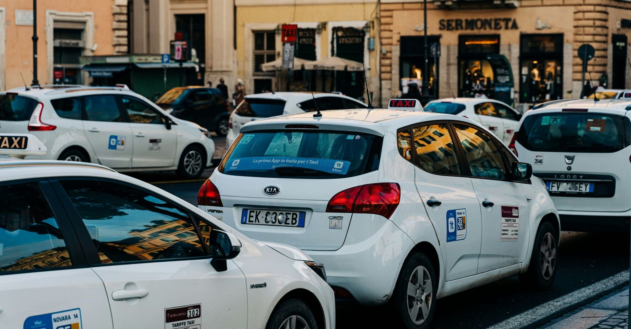 A line of white taxis waiting on a busy central Rome street during service disruption.