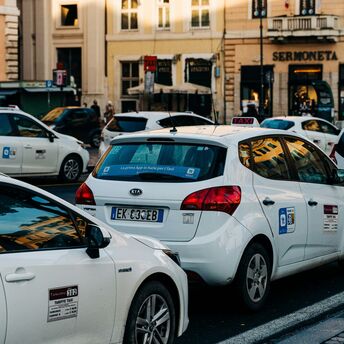 A line of white taxis waiting on a busy central Rome street during service disruption.