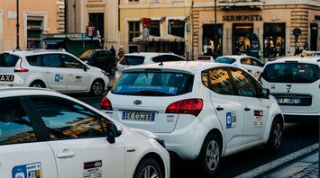 A line of white taxis waiting on a busy central Rome street during service disruption.