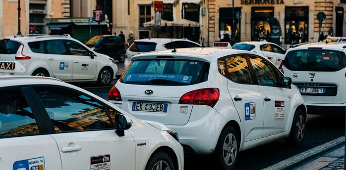 A line of white taxis waiting on a busy central Rome street during service disruption.