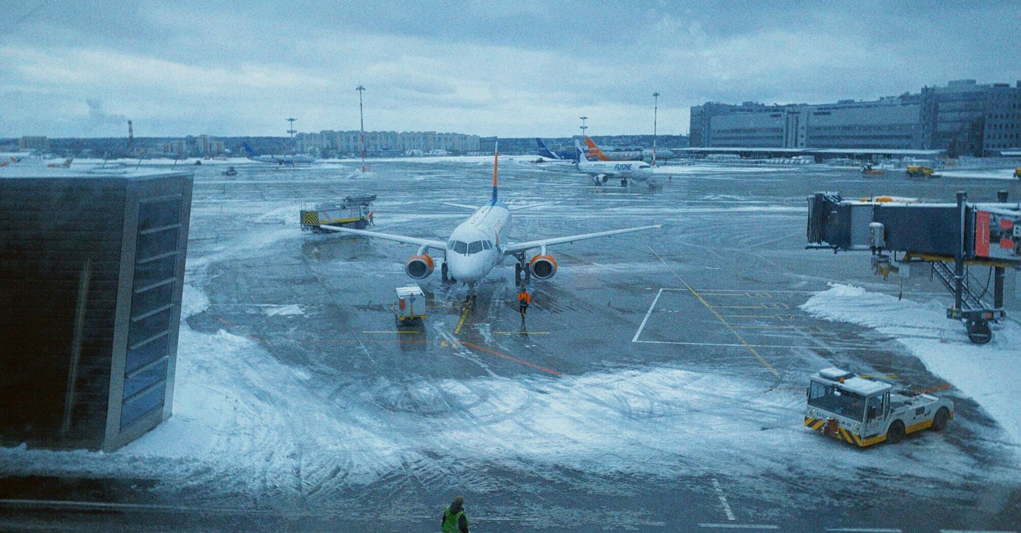 Snow-covered airport apron with grounded aircraft and staff working in icy conditions.