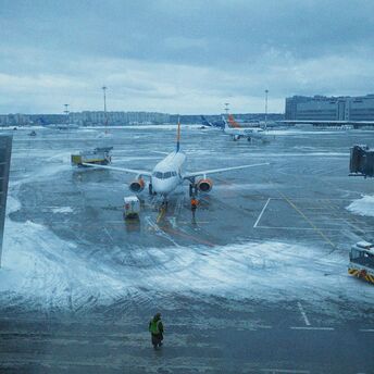 Snow-covered airport apron with grounded aircraft and staff working in icy conditions.