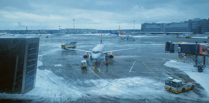 Snow-covered airport apron with grounded aircraft and staff working in icy conditions.