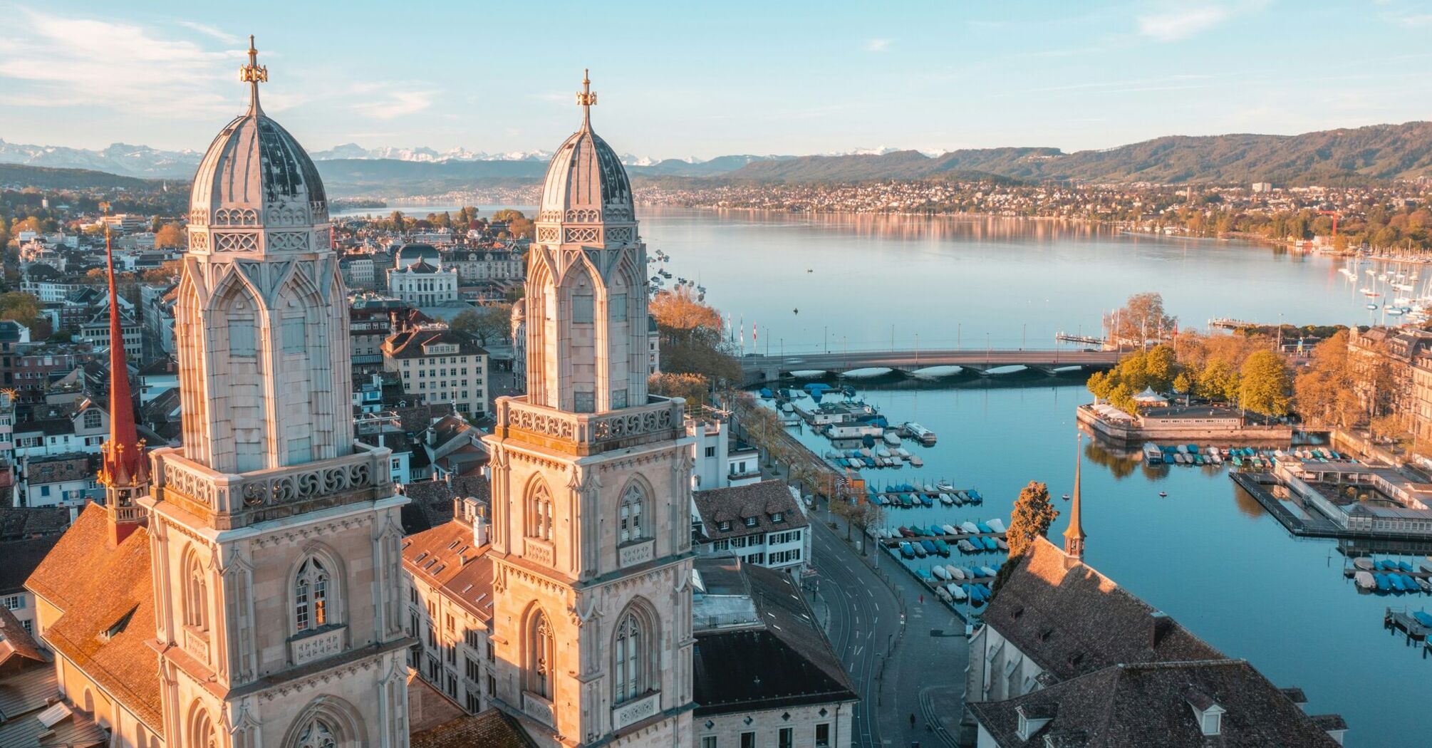 Aerial view of Zurich with lake and historic towers at sunset.