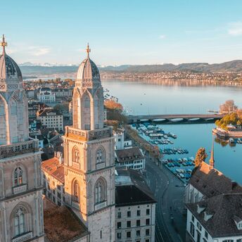 Aerial view of Zurich with lake and historic towers at sunset.