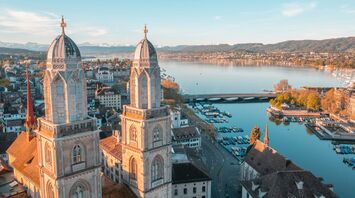Aerial view of Zurich with lake and historic towers at sunset.