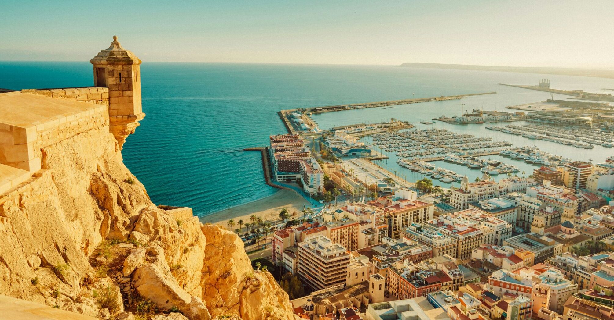 View of Alicante coastline, marina and historic fortress under clear skies