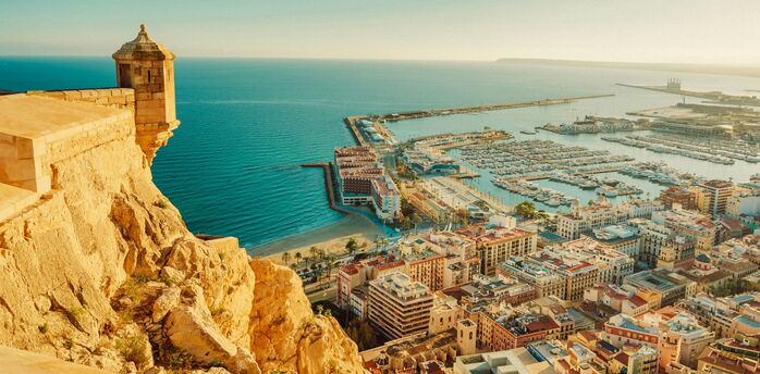 View of Alicante coastline, marina and historic fortress under clear skies