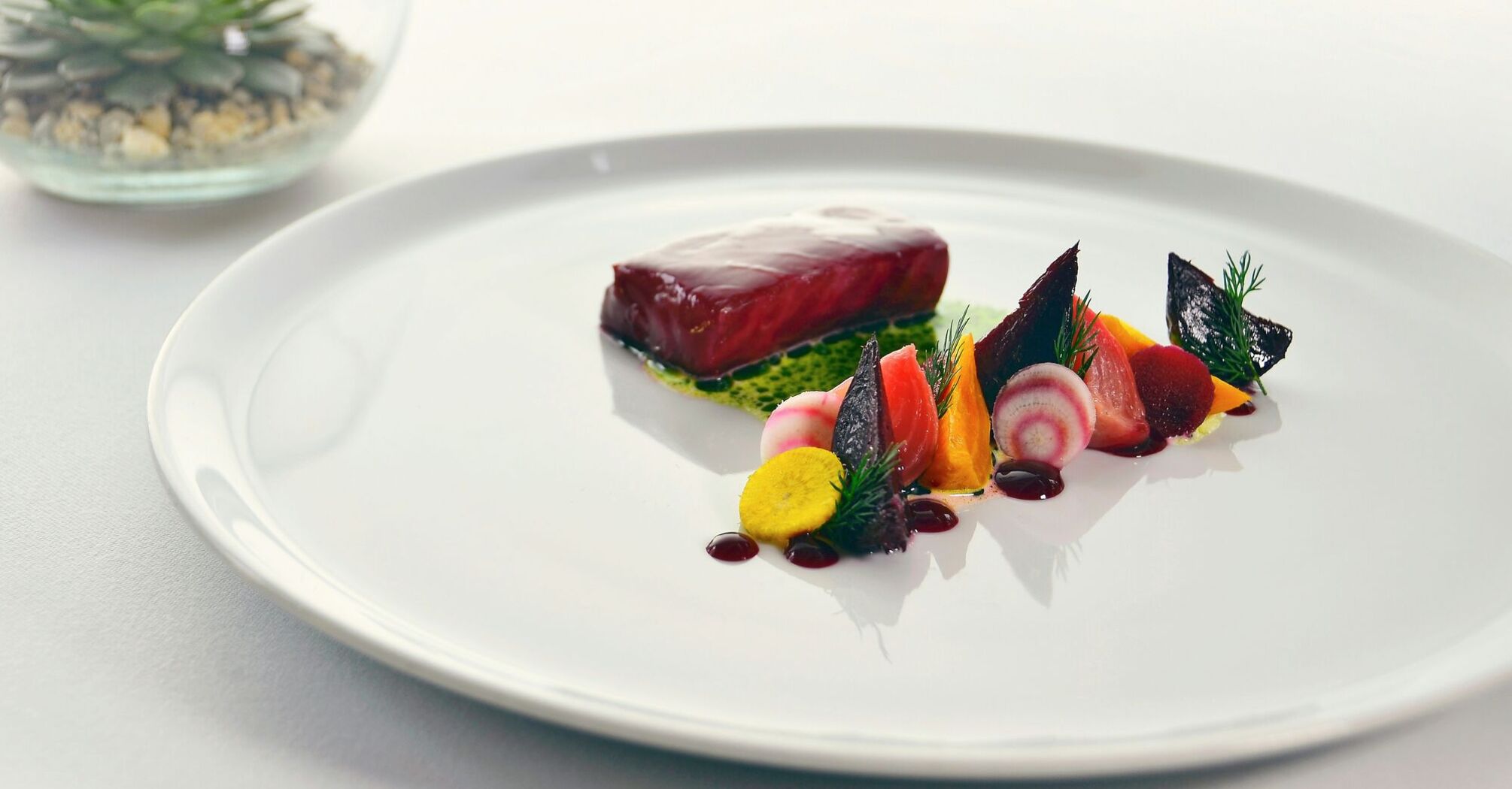 Fine dining-style plate with fish, beetroot and vegetables on a white table