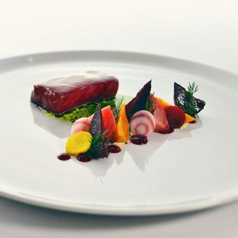Fine dining-style plate with fish, beetroot and vegetables on a white table