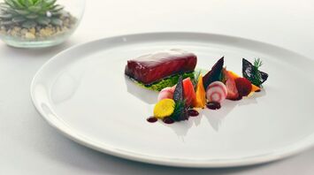 Fine dining-style plate with fish, beetroot and vegetables on a white table