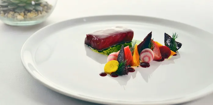 Fine dining-style plate with fish, beetroot and vegetables on a white table