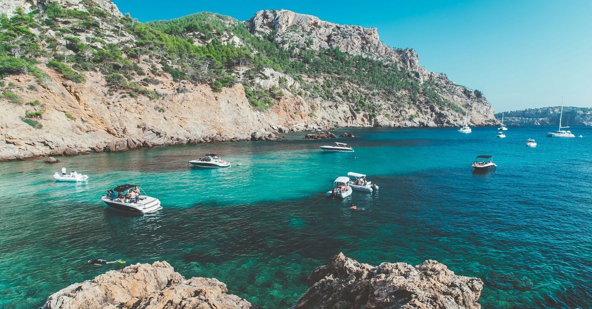 Rocky coast with boats anchored in clear turquoise water.