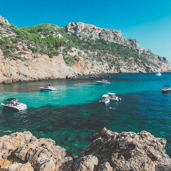 Rocky coast with boats anchored in clear turquoise water.