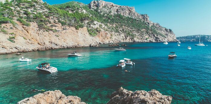 Rocky coast with boats anchored in clear turquoise water.