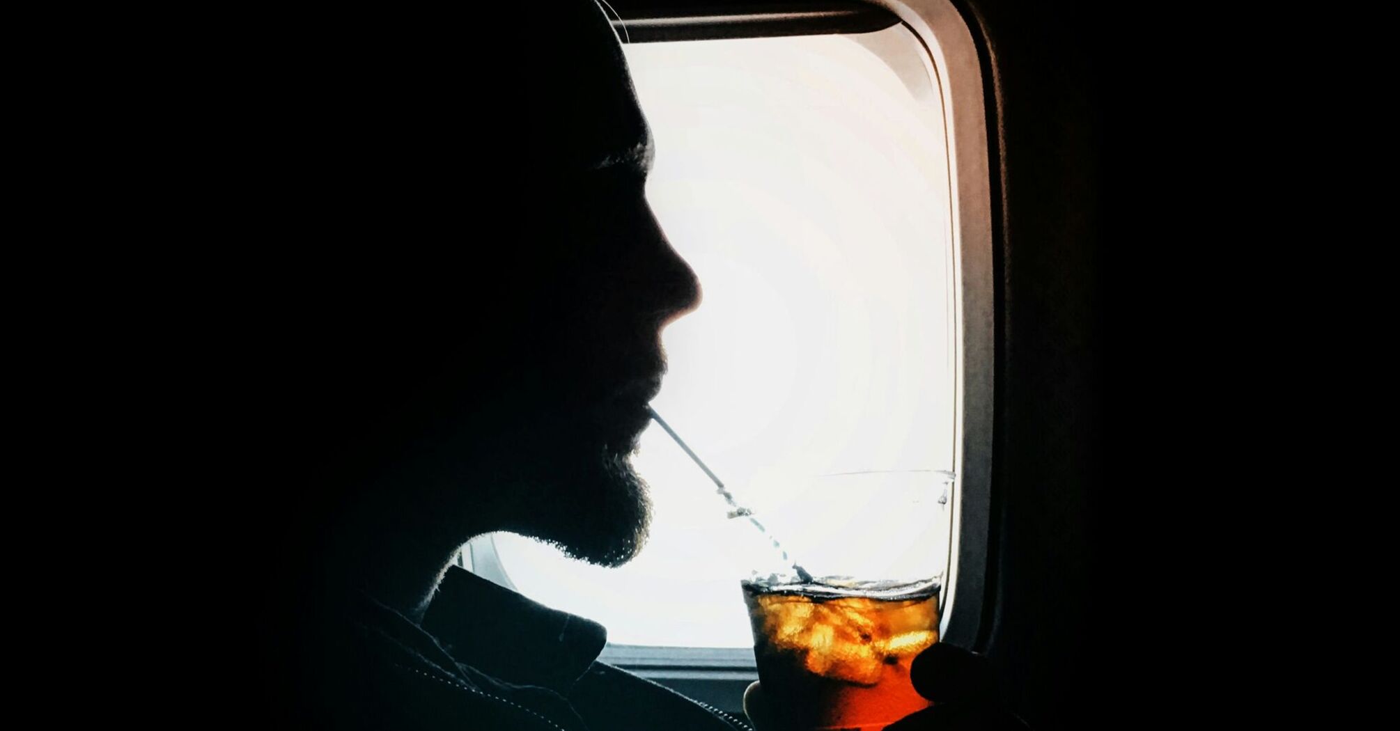 Passenger drinks a cold beverage while seated by an aircraft window