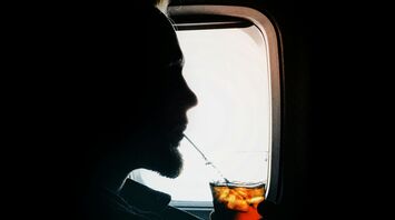 Passenger drinks a cold beverage while seated by an aircraft window