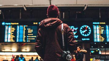 Person viewing airport departure screens with camera on shoulder
