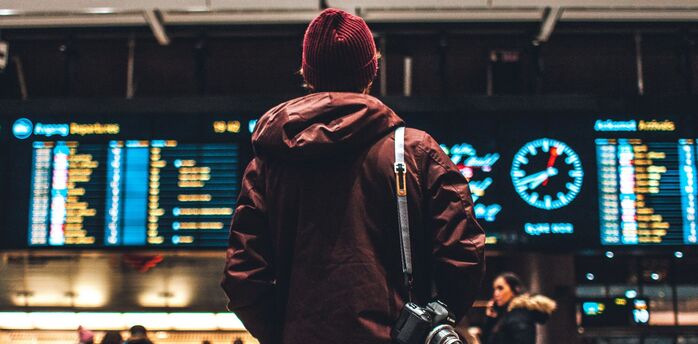 Person viewing airport departure screens with camera on shoulder