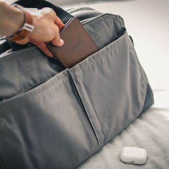 Hand placing a passport into a grey travel bag pocket