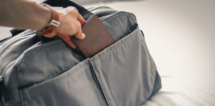 Hand placing a passport into a grey travel bag pocket