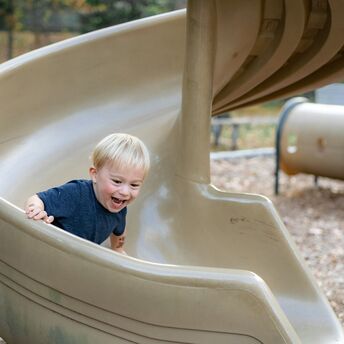 Young child smiling while sliding down a playground slide