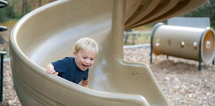 Young child smiling while sliding down a playground slide