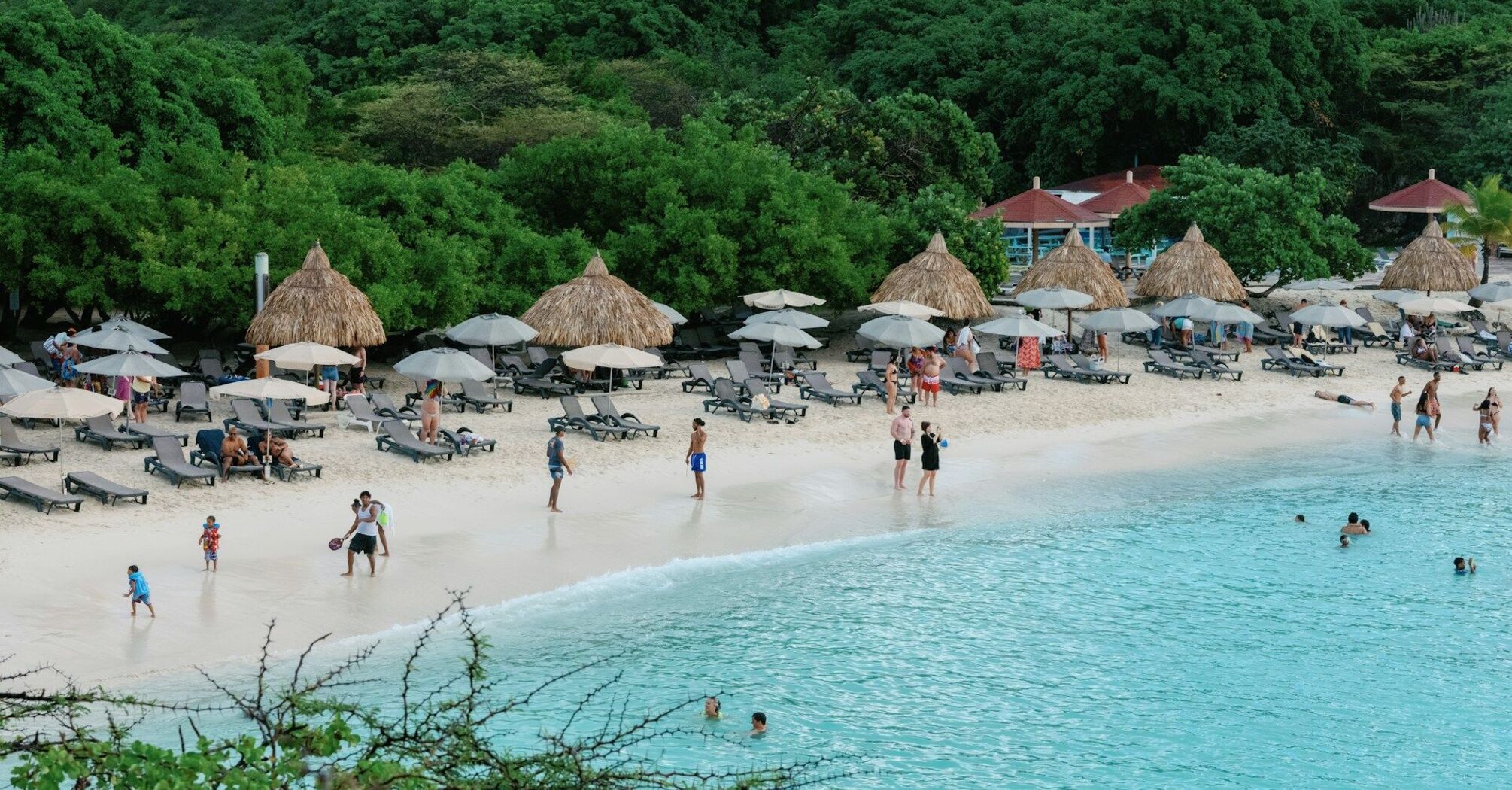 Beach with sun loungers, umbrellas and people swimming
