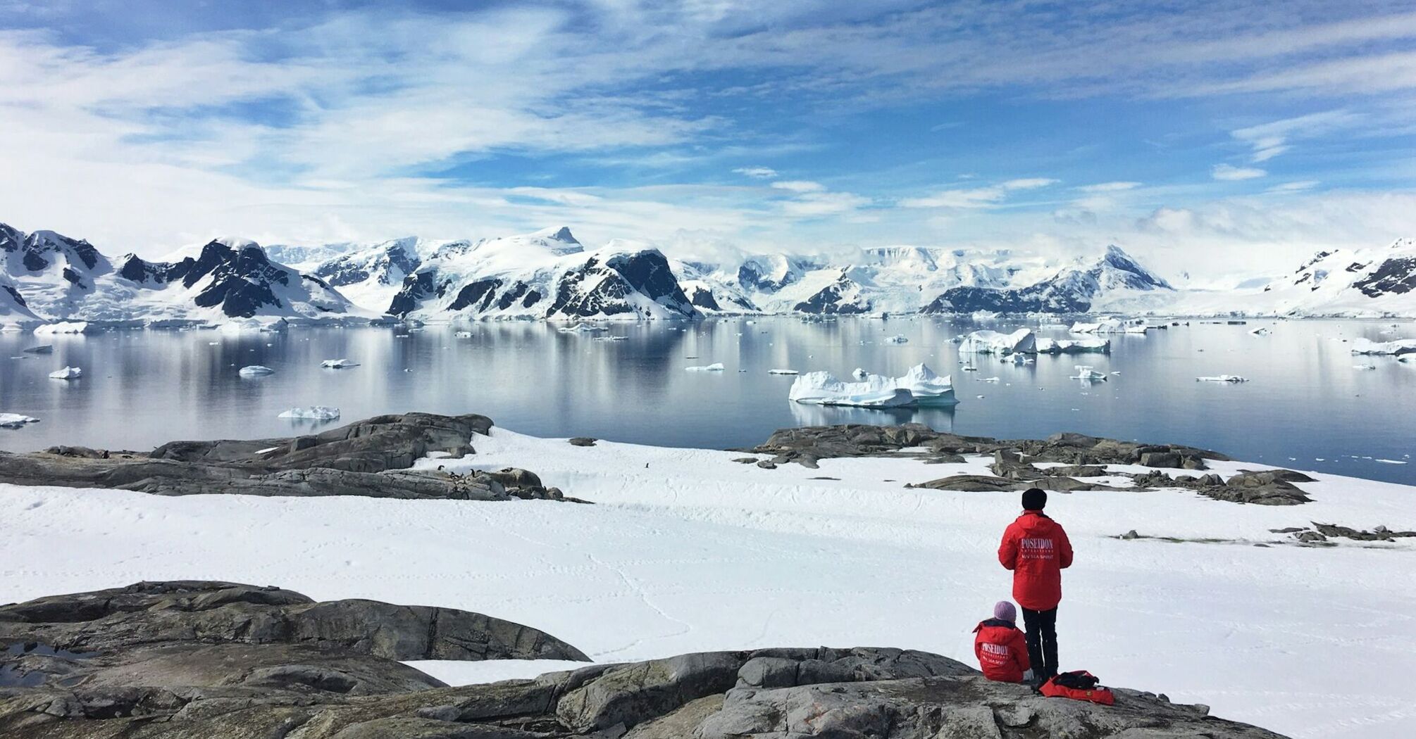 Two visitors overlooking a snowy Antarctic bay