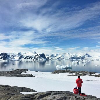 Two visitors overlooking a snowy Antarctic bay