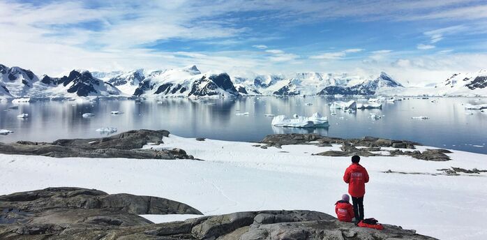 Two visitors overlooking a snowy Antarctic bay