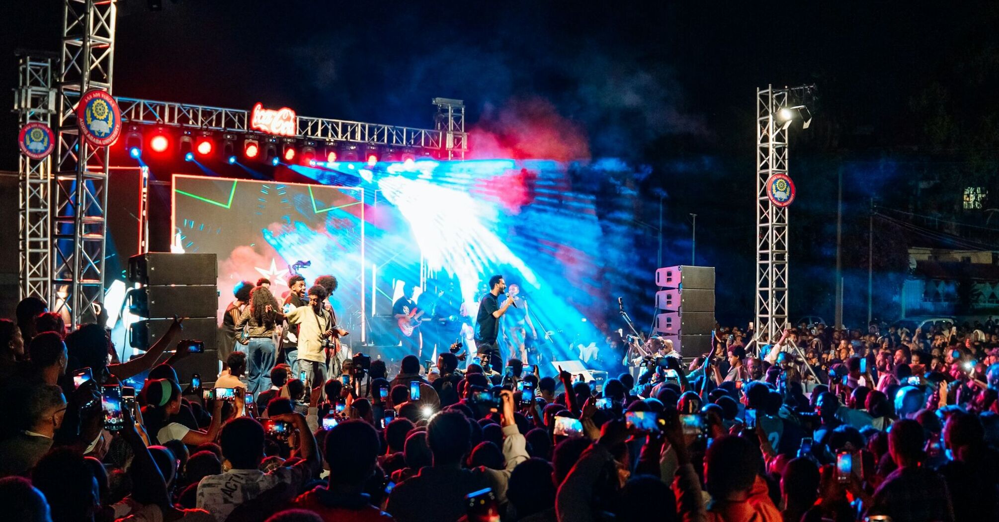 Singer performing on a brightly lit stage before a large crowd at night