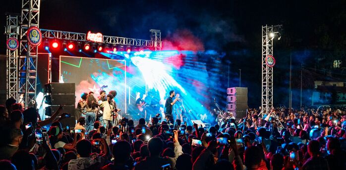 Singer performing on a brightly lit stage before a large crowd at night