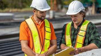 Two railway workers reviewing documents beside tracks