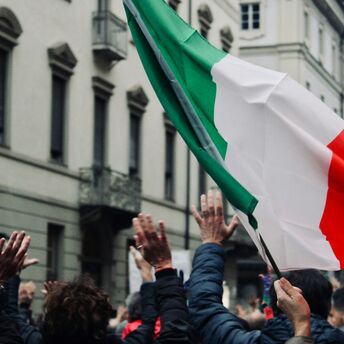 People raising their hands beneath a large Italian flag