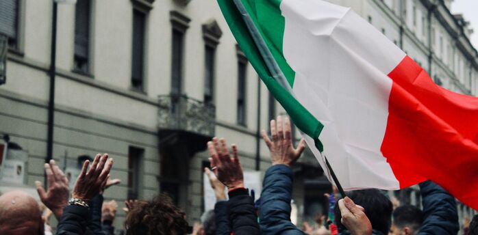 People raising their hands beneath a large Italian flag