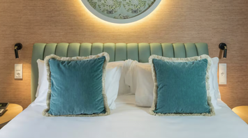 Casa Verbena Madrid bed with turquoise cushions and a decorative wall panel